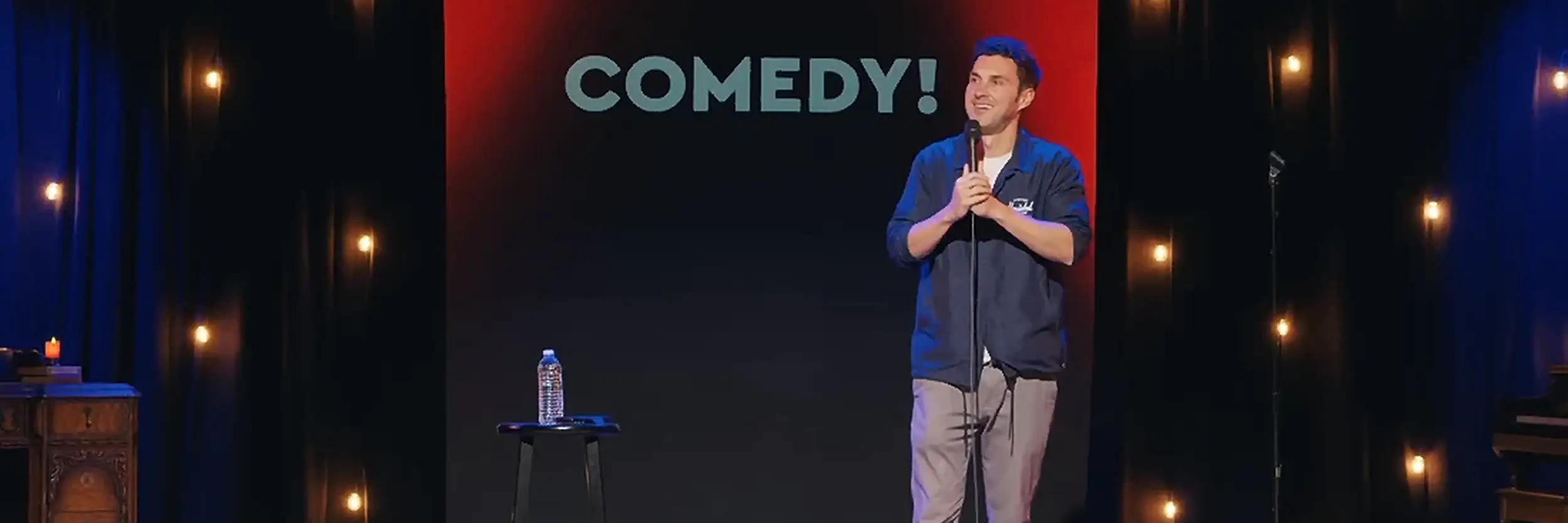 Comedy! by Mark | Mark Normand | Tuesdays with Stories Comedian Mark Normand of Tuesdays with Stories performing stand-up with a sign that says "comedy!". Find more about Mark at www.tuesdayspod.com/mark-normand